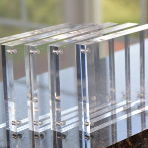 May include: Four clear acrylic picture frames with magnetic closures. The frames are stacked on top of each other.