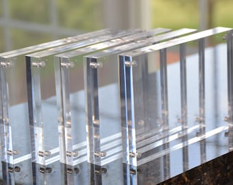 May include: Four clear acrylic picture frames with magnetic closures. The frames are stacked on top of each other.