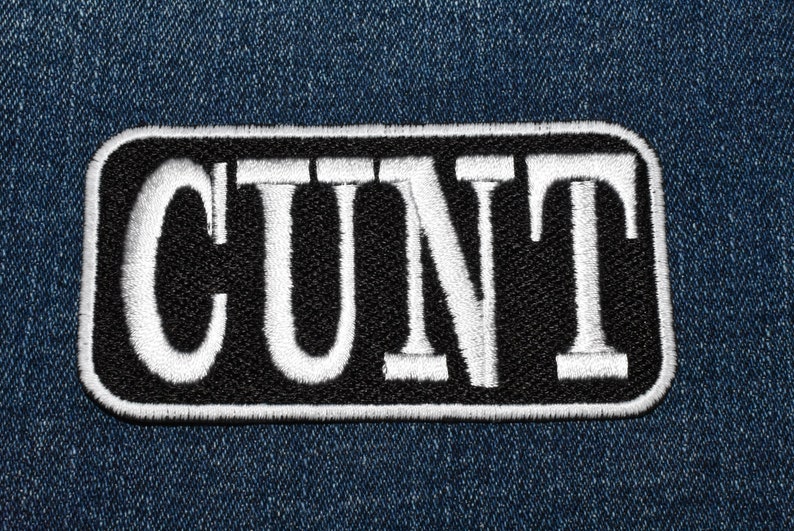 May include: A black and white embroidered patch with the word "CUNT" in white letters on a black background.