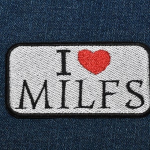 May include: A white patch with black stitching and a red heart that says "I love MILFS" on a blue denim background.