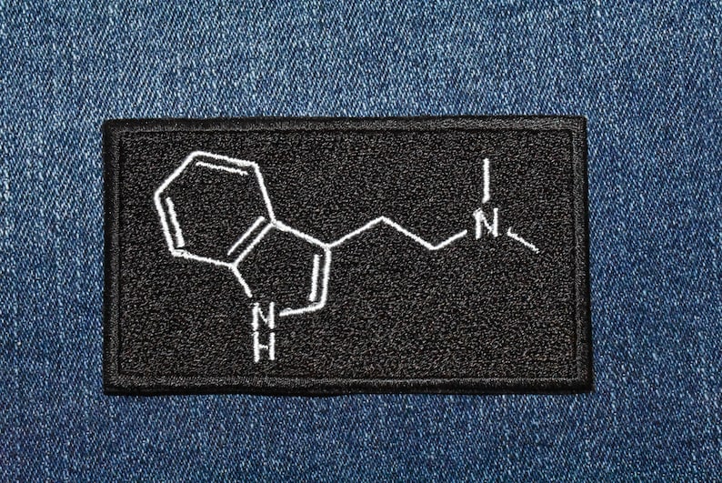 May include: Black patch with a white embroidered chemical structure of a molecule with the letters 'N' and 'H' on a denim background.