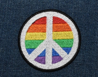 Op de afbeelding: Een regenboog vredesteken patch met een witte achtergrond en een zwarte omtrek. De patch is gemaakt van geborduurd stof en is perfect om een ​​toets van vrede en liefde toe te voegen aan je kleding of accessoires.