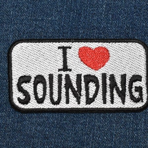 May include: A white patch with black stitching on a blue denim background. The patch says "I love sounding" with a red heart in between the words.