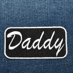 May include: A black and white embroidered patch with the word "Daddy" in a cursive font.
