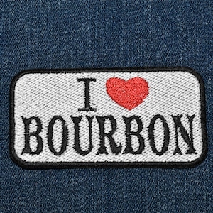 May include: A white patch with black stitching and a red heart that says "I love bourbon" on a blue denim background.
