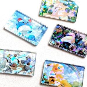 May include: Five rectangular, clear resin pieces featuring colorful cartoon characters. The characters include a blue and white creature, a yellow and brown creature, and others. Each piece has a unique background.