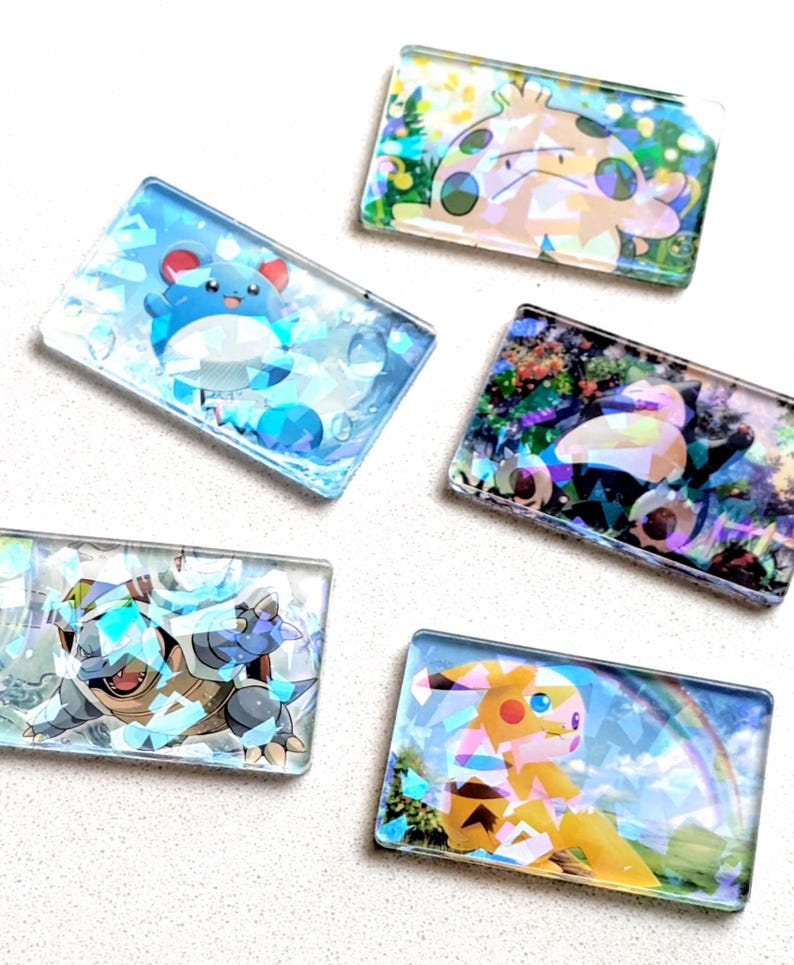 May include: Five rectangular, clear resin pieces featuring colorful cartoon characters. The characters include a blue and white creature, a yellow and brown creature, and others. Each piece has a unique background.