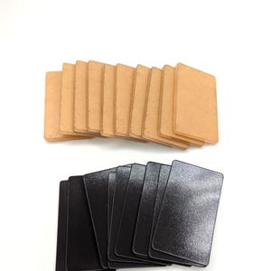 May include: Two stacks of rectangular cards on a white background. The top stack features light brown cards, while the bottom stack consists of black cards. The cards have rounded corners and a smooth surface.