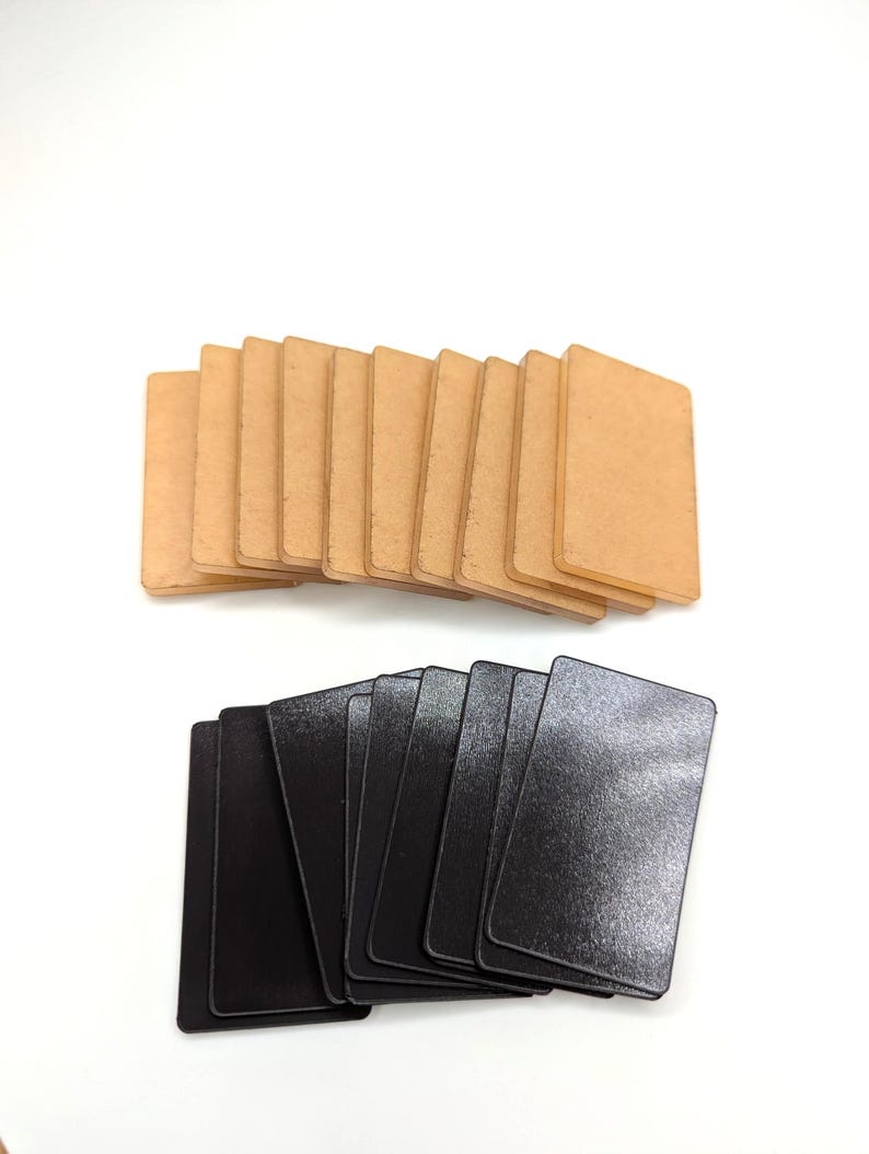 May include: Two stacks of rectangular cards on a white background. The top stack features light brown cards, while the bottom stack consists of black cards. The cards have rounded corners and a smooth surface.