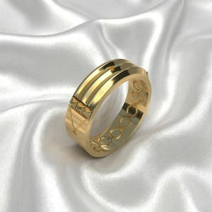 Puede incluir: Un anillo de oro con un diseño geométrico. El anillo presenta una serie de líneas paralelas y formas geométricas. La banda está grabada con símbolos de infinito. El anillo se muestra sobre una superficie blanca satinada.