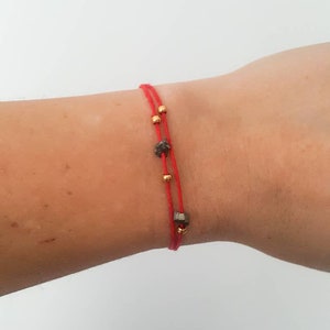 May include: A red string bracelet with gold beads and a dark gray stone charm.