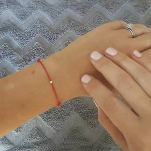 May include: A red string bracelet with a small silver bead charm.