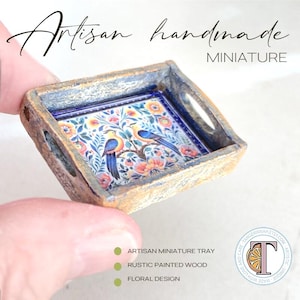 May include: A miniature wooden tray with a floral design and two birds. The tray is painted in a rustic style with a blue and white floral pattern. The tray is perfect for dollhouses or miniature scenes.