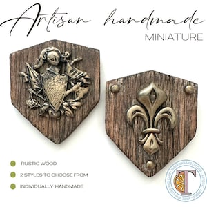May include: Two miniature wooden shields with a rustic wood finish. One shield features a knight in armor with a crest and the other features a fleur-de-lis. Both shields are individually handmade.