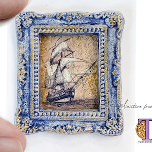 May include: A miniature framed art print of a ship with a blue and gold frame. The print is on a cream background and the ship is drawn in black ink.