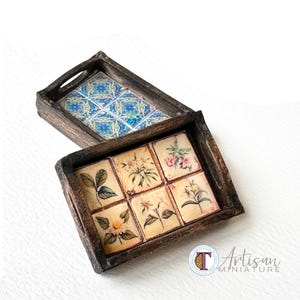 May include: Two small wooden trays. One tray features a blue and white tile design. The other tray contains six square tiles with floral illustrations. The trays are brown and have cut-out handles.
