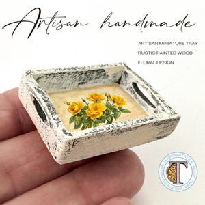 May include: A small white wooden tray with a floral design. The tray is painted with a distressed white finish and has a black floral design on the bottom. The tray is handmade and is perfect for small items.