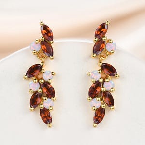 May include: A pair of gold dangle earrings with brown and white gemstones. The earrings feature a cascading design with multiple small gemstones.