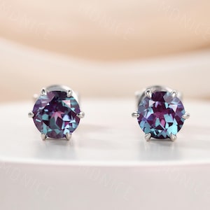 May include: A pair of silver stud earrings with round, iridescent gemstones. The gemstones have a purple and blue color with a hint of green.
