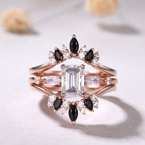 May include: A three-piece rose gold engagement ring set with a large emerald cut center stone and smaller marquise cut stones. The band features a delicate design with black and white diamonds.