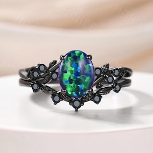 May include: A black ring set with an oval-cut opal gemstone, displaying green and blue hues. The ring features a floral design with black accents and small black gemstones, creating an elegant and nature-inspired aesthetic.