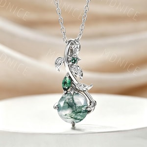 May include: A silver-toned necklace featuring a round, faceted moss agate pendant with green inclusions. The pendant is accented by a smaller marquise-cut green stone and a tiny round green stone, all set within a decorative leaf-shaped metal frame.