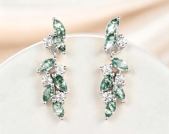 May include: A pair of silver-toned drop earrings featuring marquise-cut moss agate stones and round clear white stones arranged in a leaf-like cluster pattern. The earrings have a dangling design with multiple green patterned stones and clear accents.