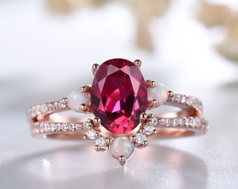 May include: A rose gold ring featuring a large oval ruby gemstone surrounded by smaller white gemstones. The ring has a delicate design with two bands and a floral motif.