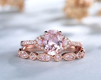May include: A rose gold engagement ring set with a large oval-shaped pink gemstone surrounded by smaller clear gemstones. The band is also set with smaller clear gemstones.