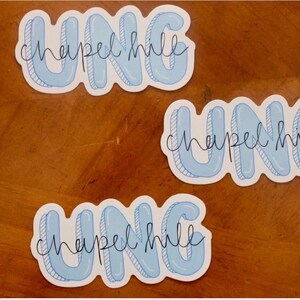 May include: Three stickers with the text "UNC Chapel Hill". The stickers have a light blue bubble letter design with a white outline and the words "Chapel Hill" in a cursive font.