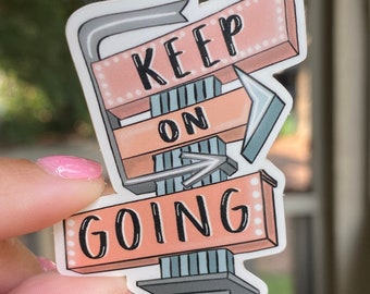 Può includere: Un adesivo rosa e bianco con un design di segnaletica retrò che recita "Keep on Going". Il segnale ha una freccia grigia che punta a destra e una freccia argentata che punta a sinistra. L'adesivo ha un bordo bianco e un simbolo di copyright in basso.