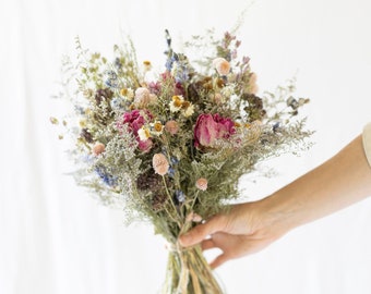 Könnte beinhalten: Ein Strauß getrockneter Blumen in Rosa-, Weiß- und Blautönen, gebunden mit Schnur. Der Strauß enthält getrocknete Rosen, Gänseblümchen und andere Wildblumen.