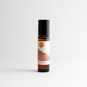 May include: A brown glass roller bottle with a black cap and a white label. The label features a graphic of a sunset over a desert landscape with the text "SANDALWOOD, CLARY SAGE".