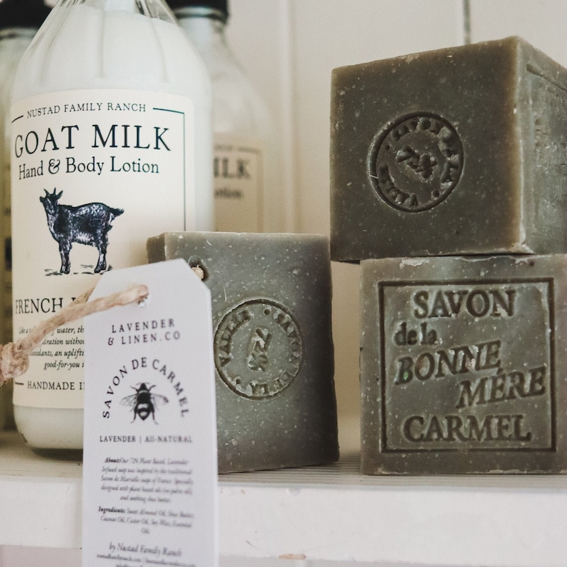 Puede incluir: Una variedad de jabones hechos a mano y loci&oacute;n de leche de cabra. Los jabones son de color verde apagado, algunos con dise&ntilde;os y texto en relieve. Una etiqueta dice "Lavender & Linen Co. Savon de Carmel". Se ve una botella de loci&oacute;n de leche de cabra.