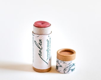 Bálsamo labial natural, teñido con hibisco y arcilla rosa, infusionado con manteca de karité batida y aceite de almendras dulces.