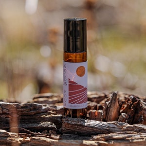 Może przedstawiać: Brązowa szklana butelka z rolką z czarną zakrętką i białą etykietą z napisem "Golden Hour Chamomile Lavender Roll-On". Etykieta zawiera grafikę zachodu słońca nad pasmem g&oacute;rskim.