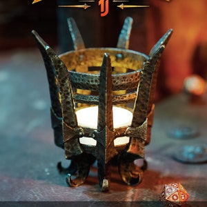 May include: A black metal tealight brazier with a decorative design. The brazier is lit with a candle and sits on a rustic surface. The text "SHADOW FORGED" is displayed above the brazier.