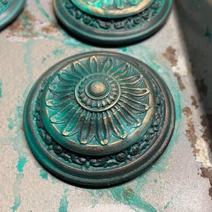 Peut inclure: Quatre ornements ronds d&eacute;coratifs de couleur vert sarcelle et or avec des motifs floraux complexes. Les ornements ont un centre sur&eacute;lev&eacute; avec un cercle plus petit au centre.