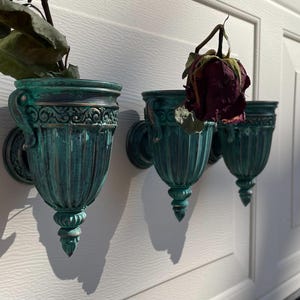 Peut inclure: Trois pots muraux en vert sarcelle avec des d&eacute;tails orn&eacute;s. Les pots sont vides, mais l'un contient une rose s&eacute;ch&eacute;e.