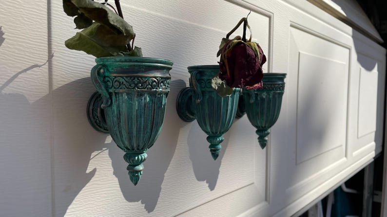 Peut inclure: Trois pots muraux en vert sarcelle avec des d&eacute;tails orn&eacute;s. Les pots sont vides, mais l'un contient une rose s&eacute;ch&eacute;e.