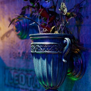 Peut inclure: Un vase orn&eacute; bleu et or avec un arrangement floral de fleurs bleues et violettes. Le vase est mont&eacute; sur un mur et porte le texte "The Mourner's Vase" en dessous.