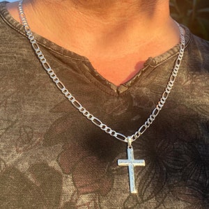 May include: A silver chain necklace with a silver cross pendant. The chain is a figaro style chain.