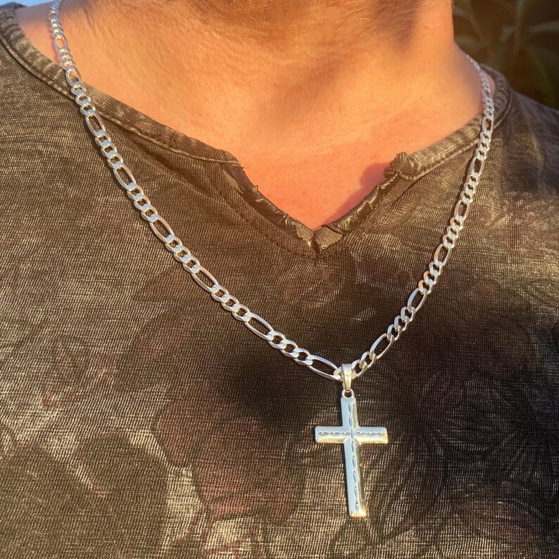 May include: A silver chain necklace with a silver cross pendant. The chain is a figaro style chain.