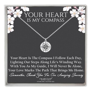 May include: A sterling silver necklace with a compass pendant. The pendant hangs from a delicate chain and features a compass rose design. The card behind the necklace has the text "YOUR HEART IS MY COMPASS".