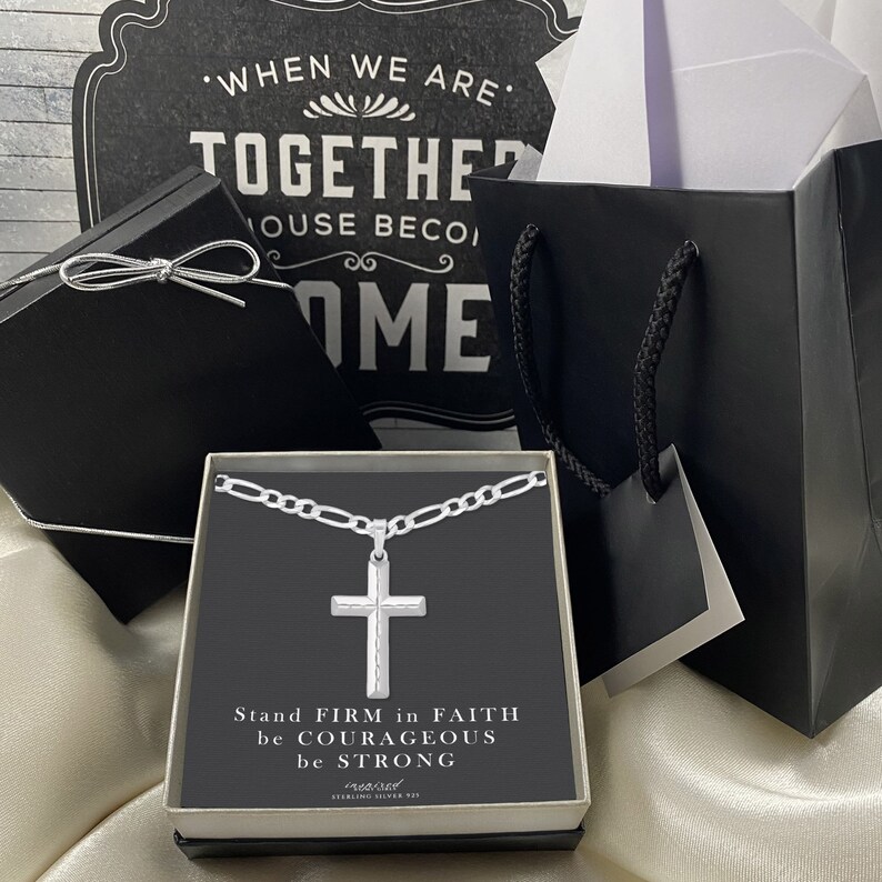 May include: A silver chain necklace with a silver cross pendant in a black box. The box has a white background with the text "Stand FIRM in FAITH be COURAGEOUS be STRONG" and "Sterling Silver 925".