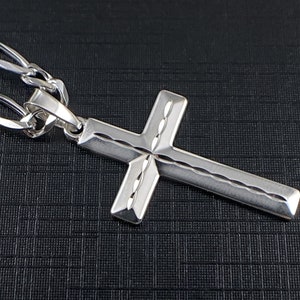 May include: A silver cross pendant with a detailed, textured design. The cross is attached to a silver chain.