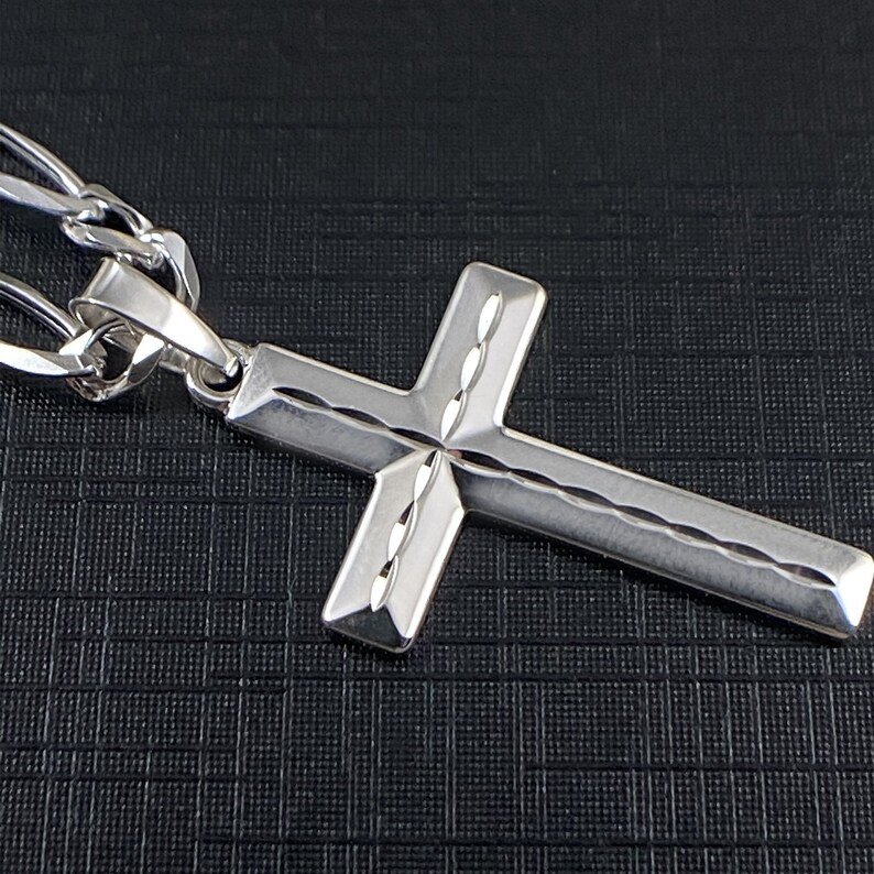 May include: A silver cross pendant with a detailed, textured design. The cross is attached to a silver chain.