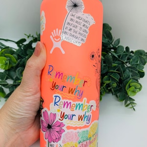 May include: A coral water bottle decorated with stickers. The stickers display floral designs, motivational quotes, and the words "Remember your why." The bottle has a black handle and lid.