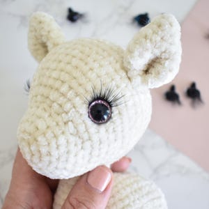 Puede incluir: Un animal de peluche blanco de crochet con pesta&ntilde;as negras y ojos negros con borde rosa. El animal tiene orejas grandes y una nariz peque&ntilde;a.