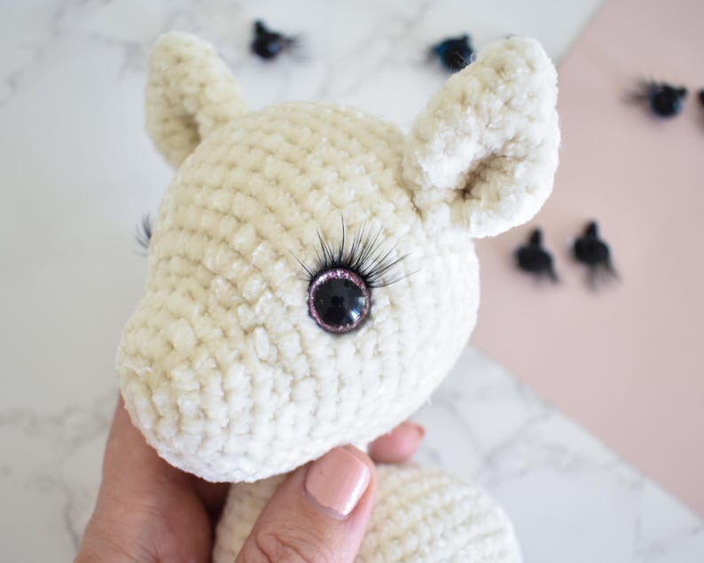 Puede incluir: Un animal de peluche blanco de crochet con pesta&ntilde;as negras y ojos negros con borde rosa. El animal tiene orejas grandes y una nariz peque&ntilde;a.